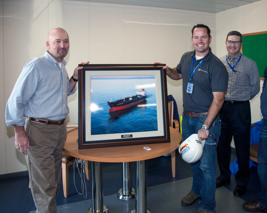 A framed photo of the Lone Star State is presented by Pete Radzicki, program manager for NASSCO's ECO program, to David Farrell, project manager for American Petroleum Tankers. In the background: Kevin Graney, vice president and general manager for General Dynamics NASSCO.